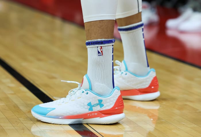 View of white, teal, and orange Under Armour shoes.